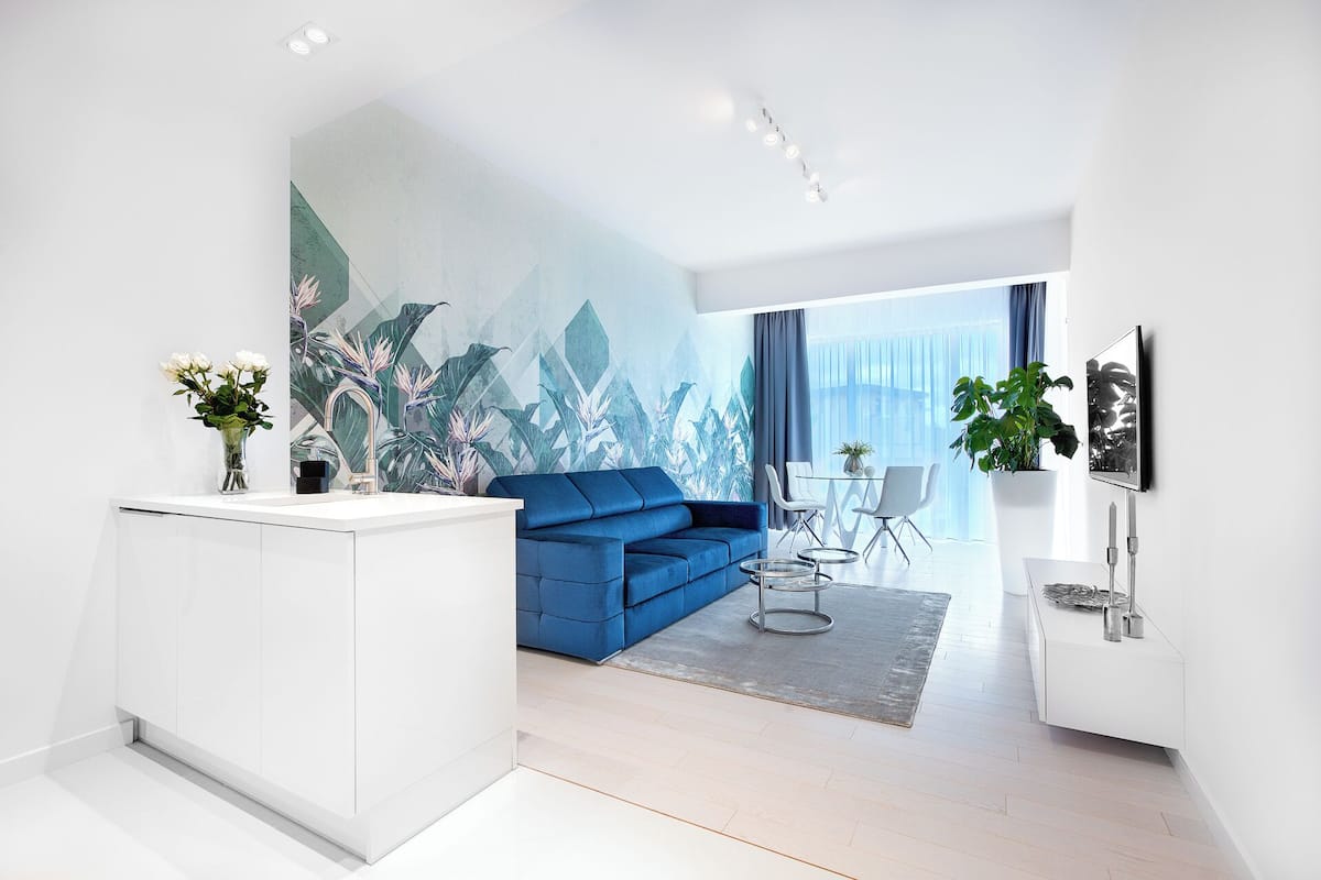 Ein modernes Wohnzimmer mit einem blauen Sofa, weißen Schränken und einem großen tropischen Wandbild.