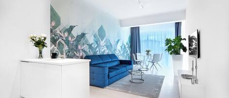 Ein modernes Wohnzimmer mit einem blauen Sofa, weißen Schränken und einem großen tropischen Wandbild.