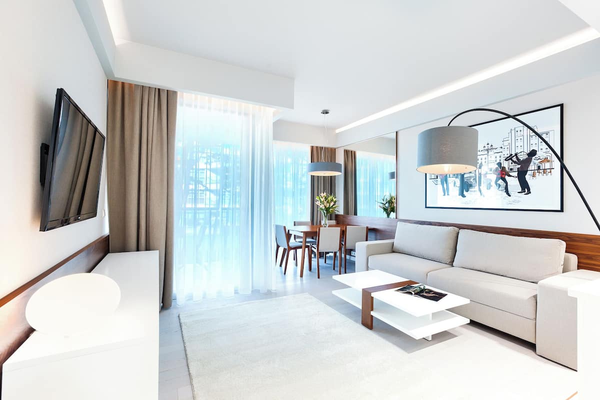 Ein modernes Hotelzimmer mit einer Couch, einem Couchtisch und einem Essbereich mit Tisch und Stühlen.