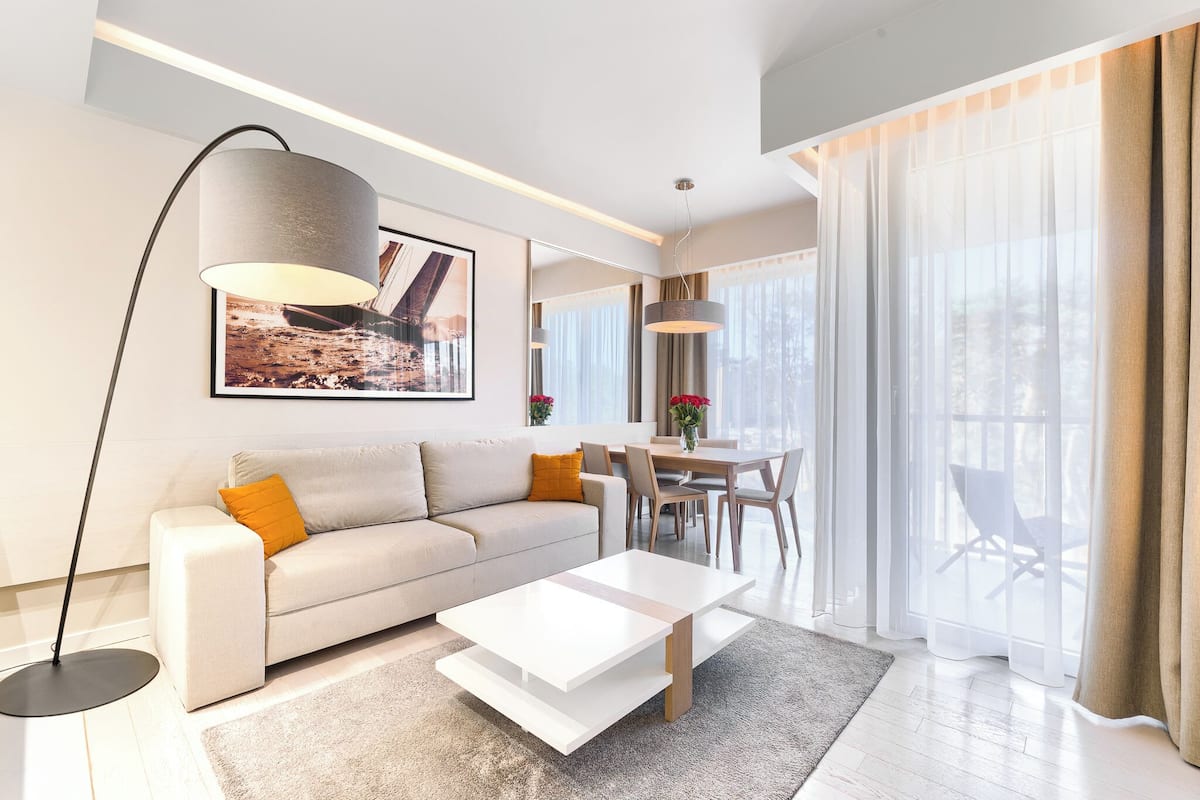 Ein modernes Wohnzimmer mit einer Couch, Couchtisch und Stehlampe. Es gibt einen Essbereich mit Stühlen und einem Tisch.