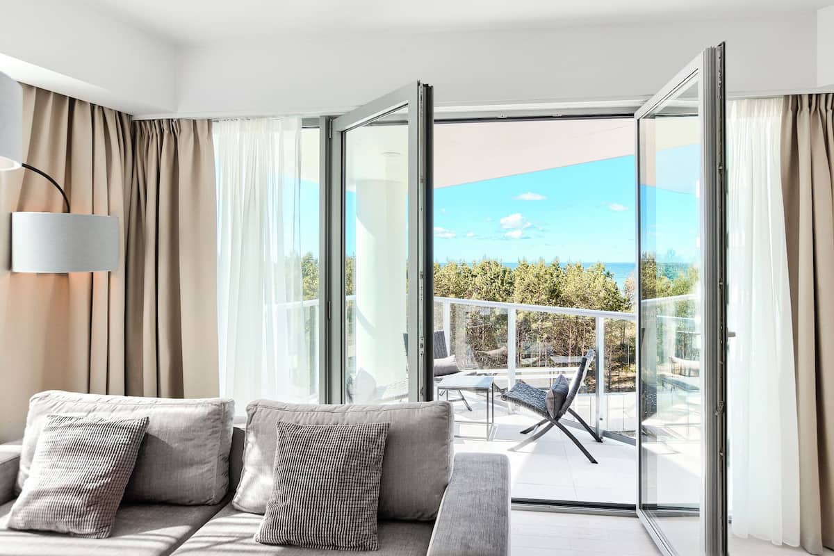 Ein modernes Wohnzimmer mit einer Couch, einer Lampe und Blick auf einen Balkon mit Gartenmöbeln.