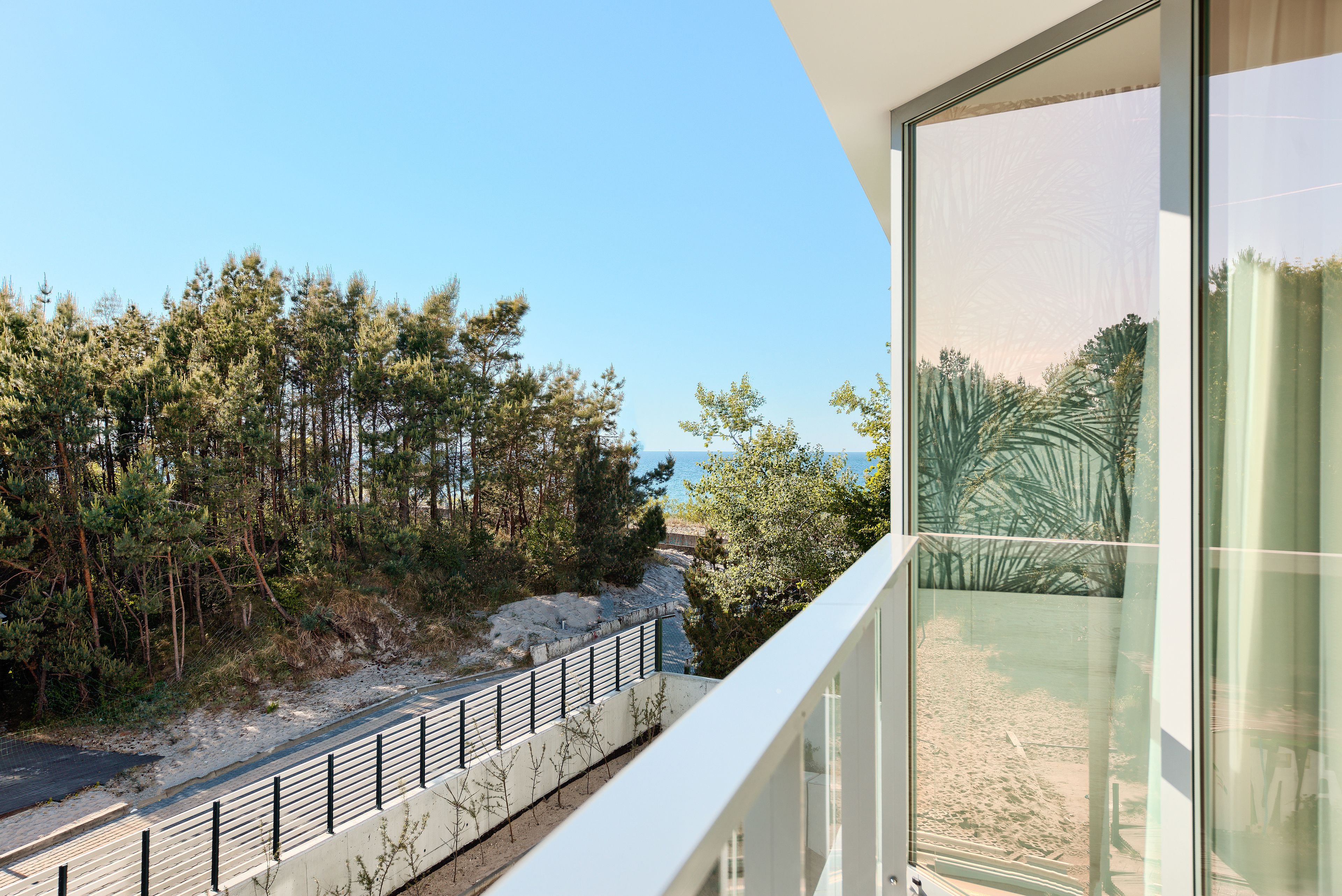 Een modern gebouw met een groot raam met uitzicht op een strand en bos.