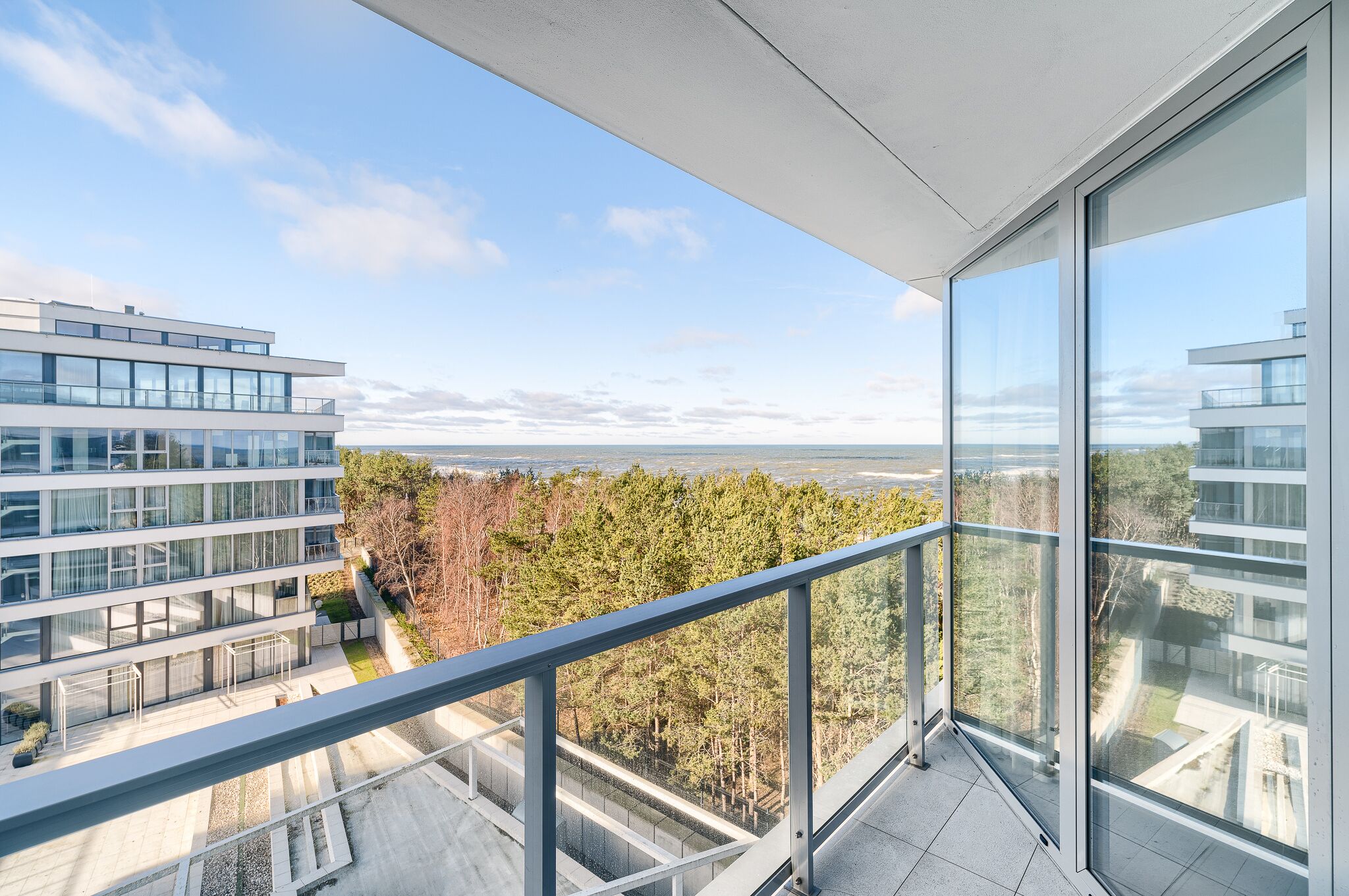 A modern building with large windows and a balcony overlooking a forested area.