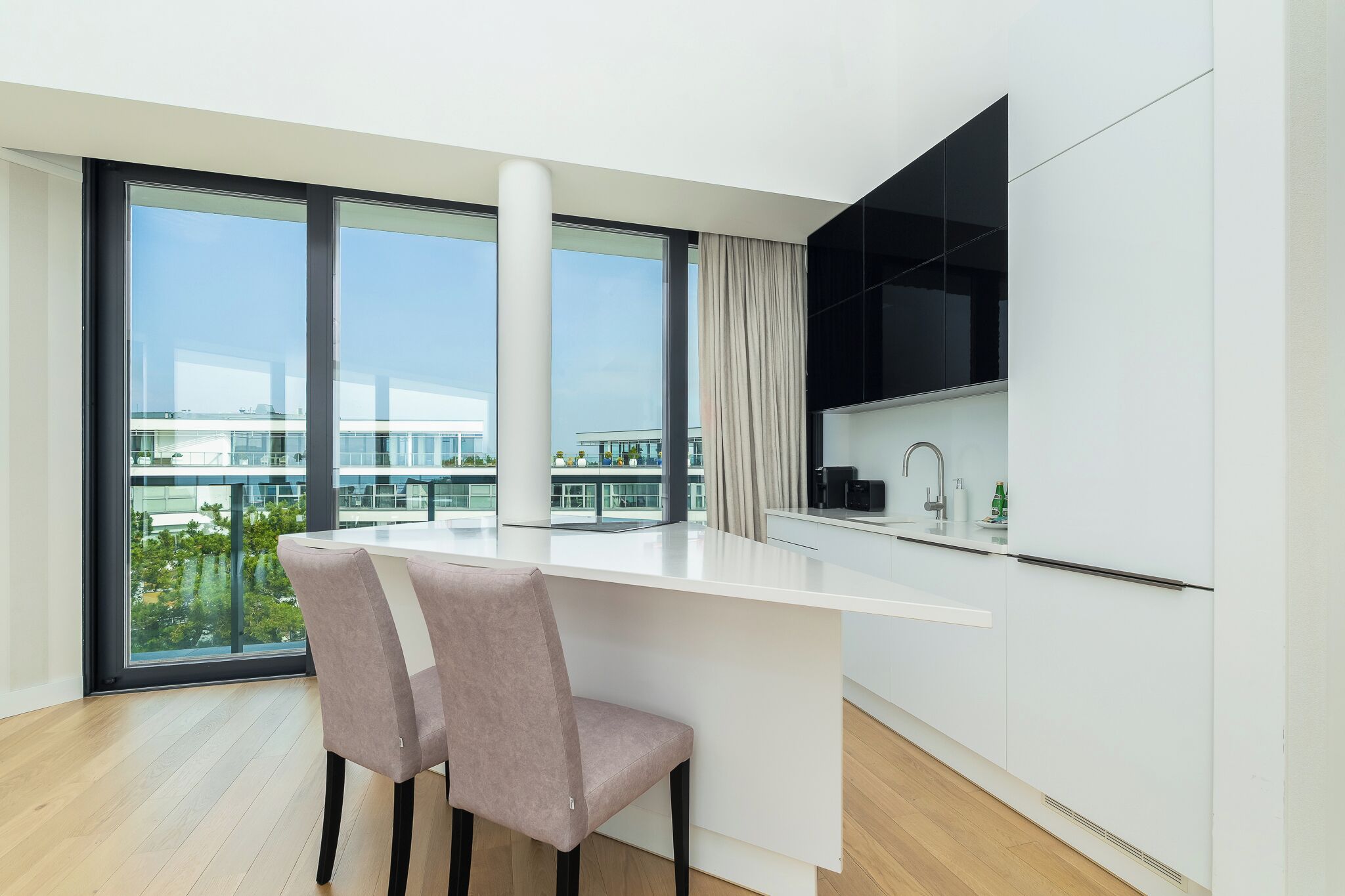 A modern kitchen with a large window, a white countertop, and a chair.