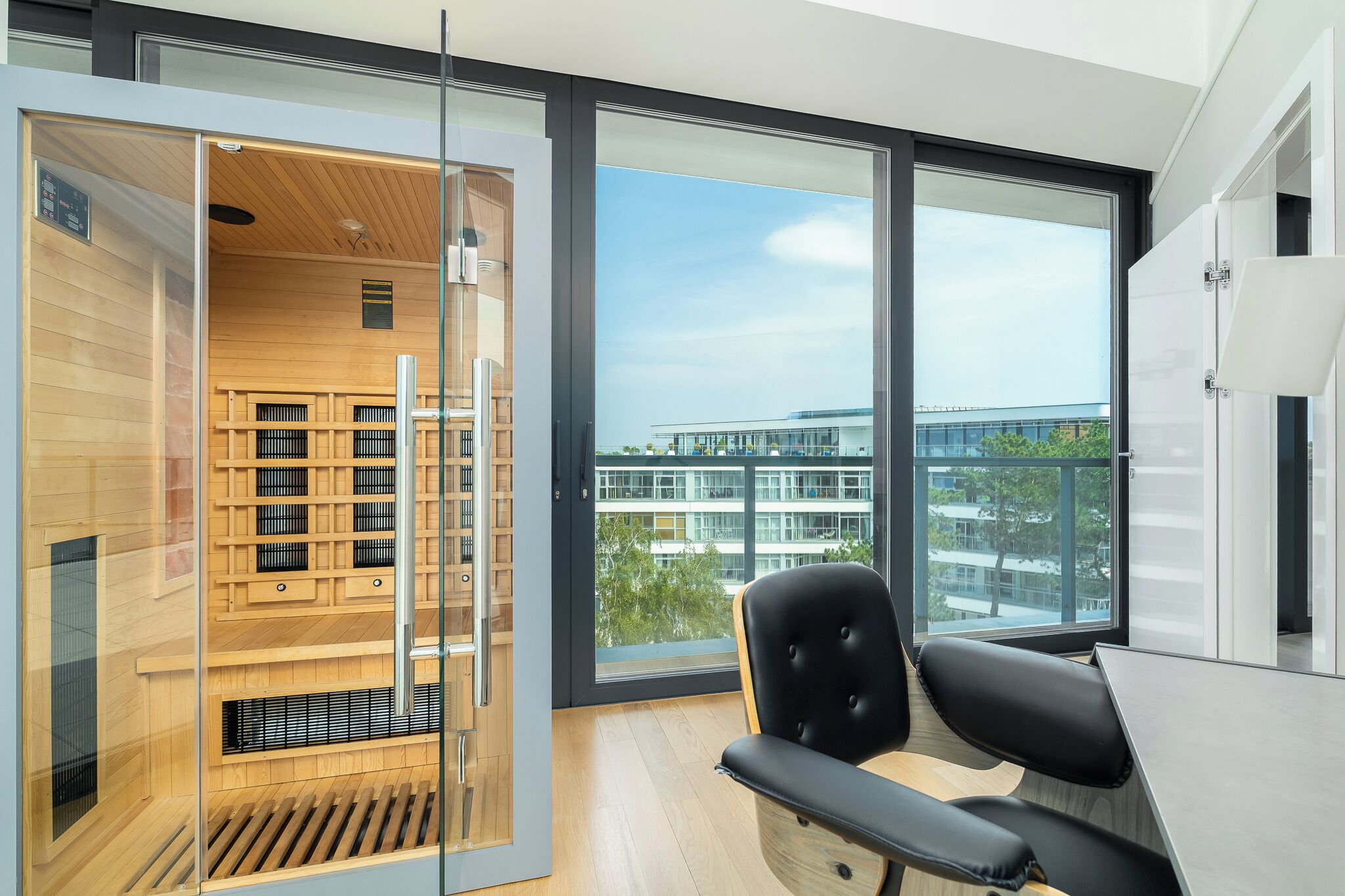 A modern room with a large window, a wooden sauna, a black chair, and a wooden desk.