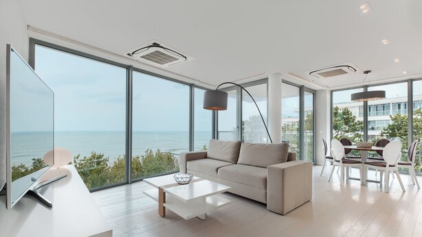 Una sala de estar moderna con un ventanal grande con vista al mar, un sofá, una mesa de centro y un comedor con sillas.