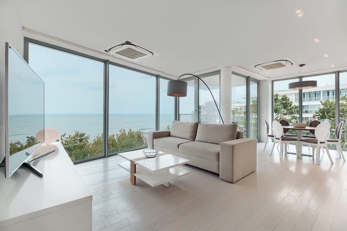 Ein modernes Wohnzimmer mit großem Fenster mit Blick auf das Meer, einer Couch, einem Couchtisch und einem Essbereich mit Stühlen.
