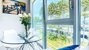 Una habitación moderna con una mesa de vidrio, sillas blancas, un florero con flores blancas y un cuadro de una playa.