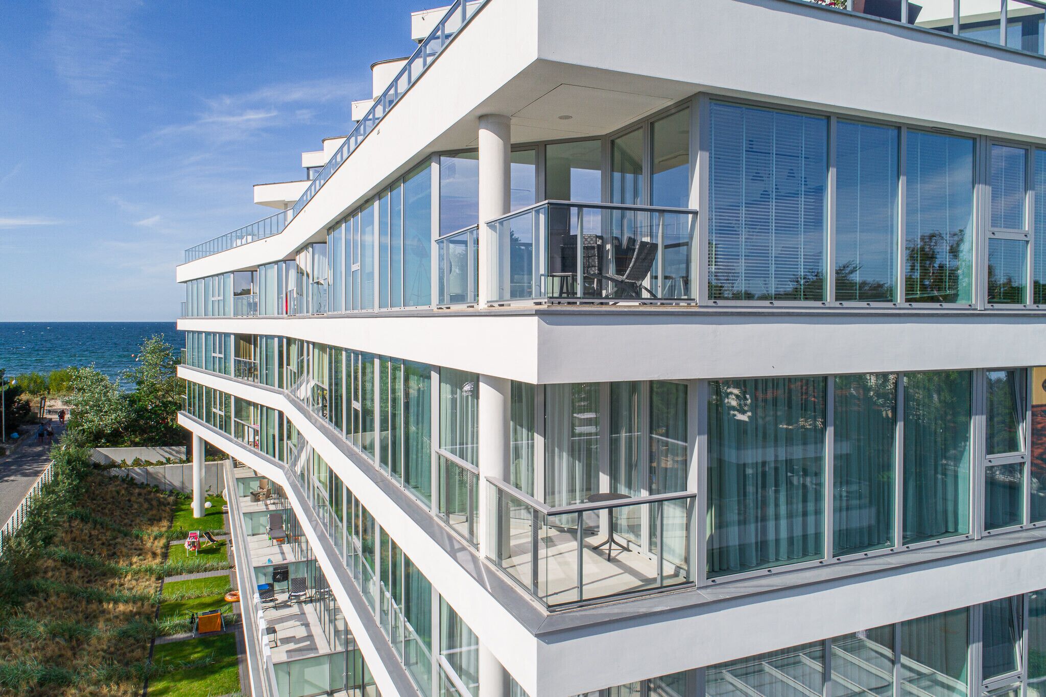 A modern multi-story building with large glass windows and balconies, overlooking a body of water.