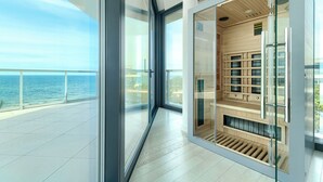 Un interior moderno con ventanas amplias, una puerta de cristal que da a un área de almacenamiento de madera y vistas al mar.