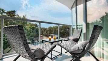 A balcony with wicker chairs and a table, two glasses of orange juice, and a view of trees and buildings.