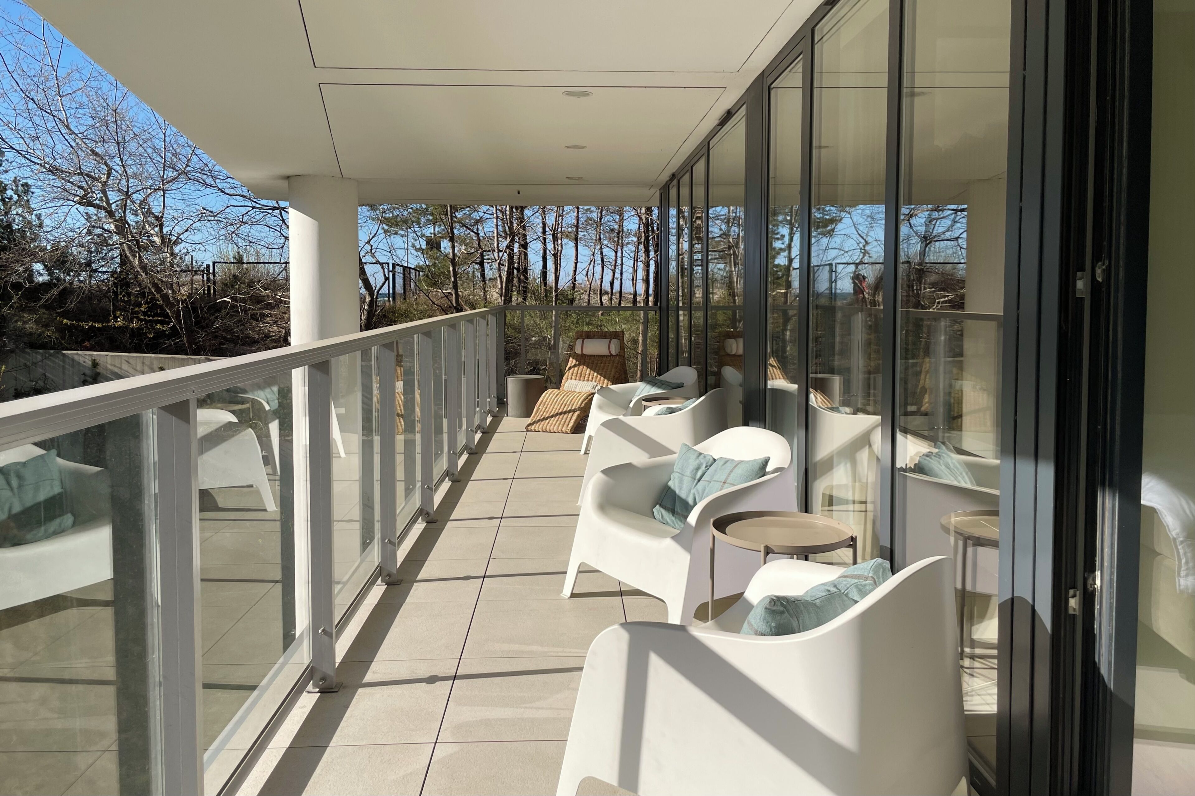 Un balcon avec des chaises blanches et une table, une balustrade en verre et une vue sur les arbres.