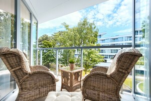 Un balcón con mobiliario de mimbre y una mesa de vidrio, con vista a un edificio y árboles.