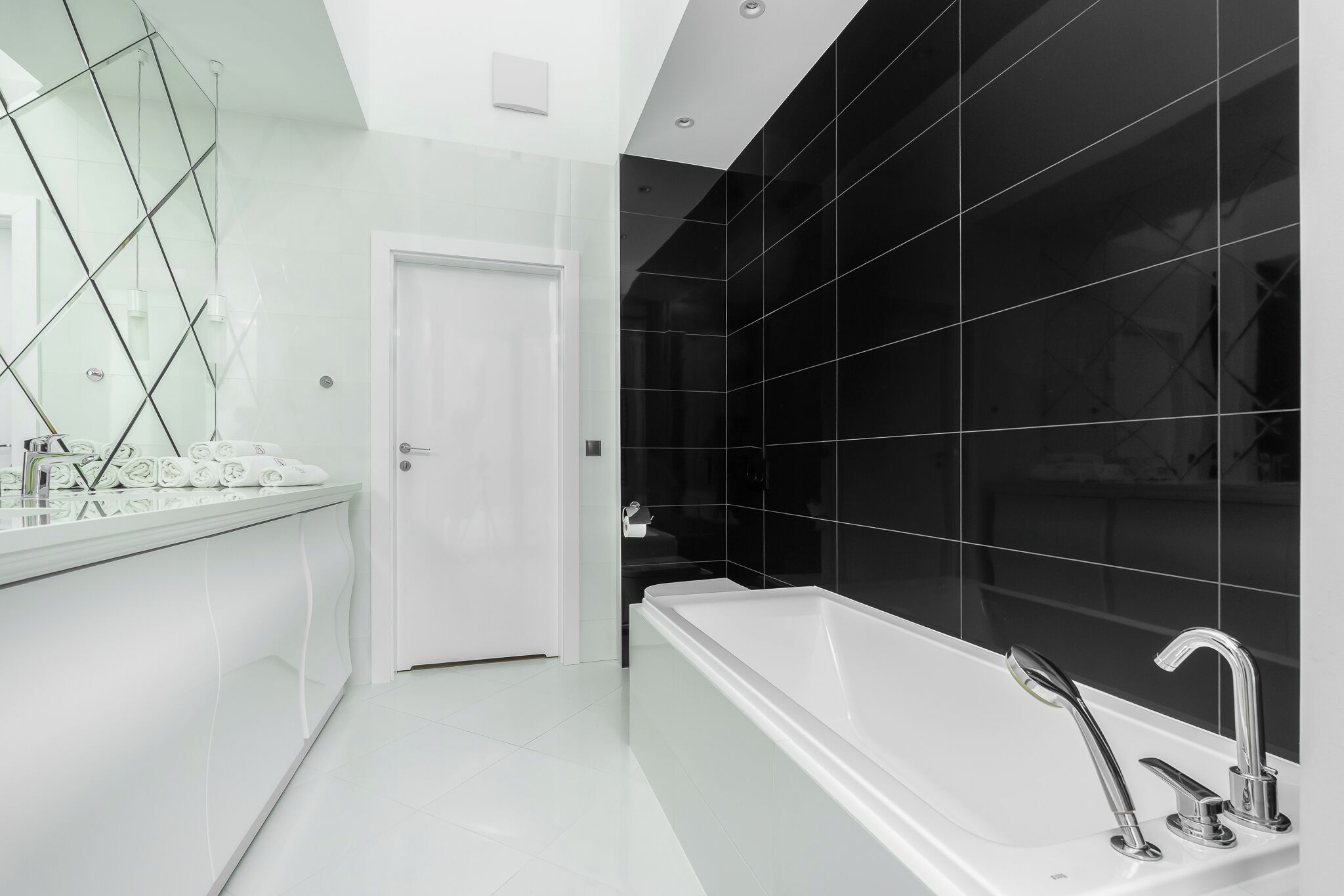 A modern bathroom with a white bathtub, a large mirror, and a door leading to another room.