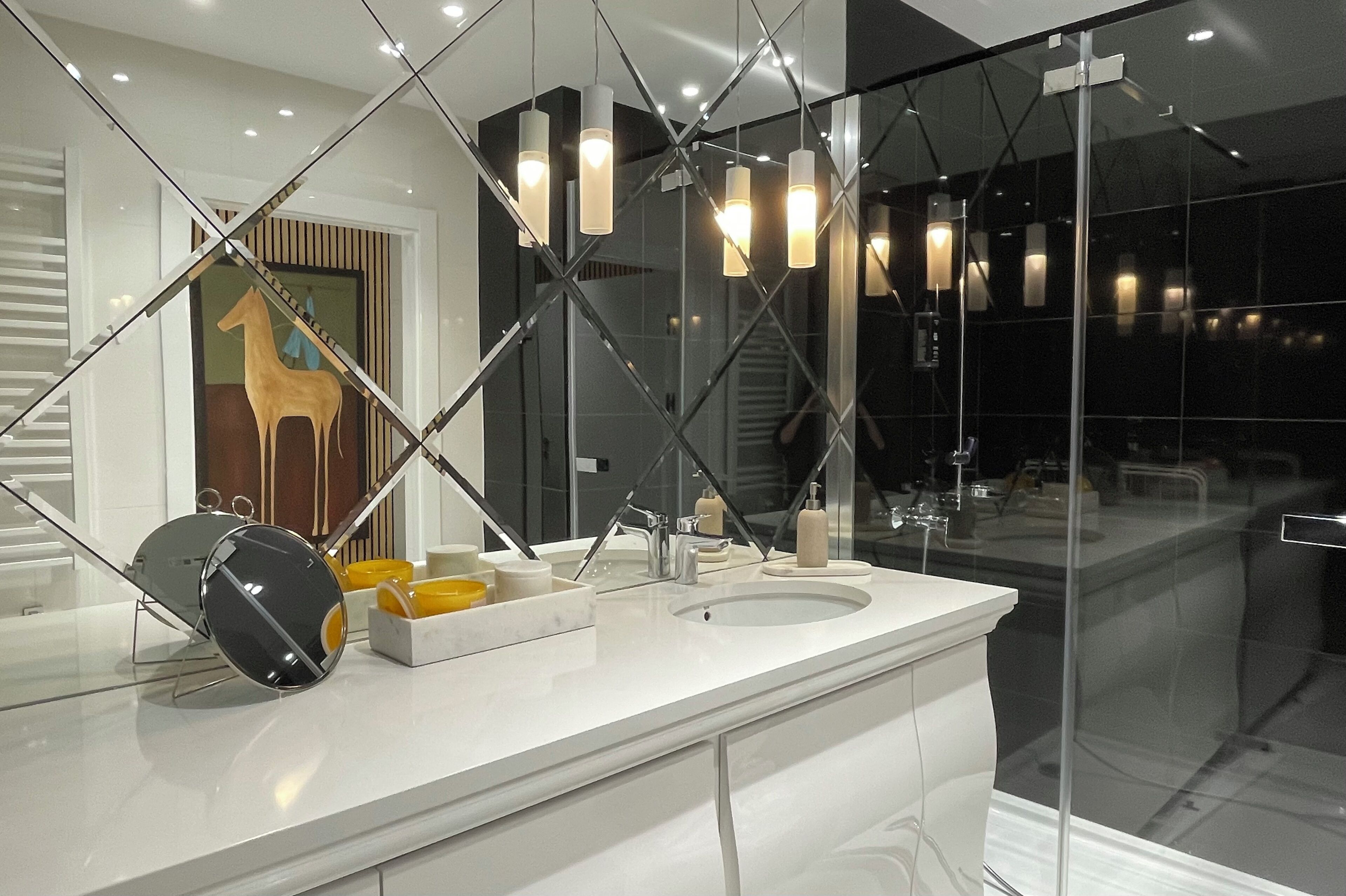 A modern bathroom with a large mirror, a round mirror, a white sink, and a glass shower enclosure.