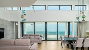 Amplia sala de estar con un gran ventanal con vista al mar, una mesa de comedor con sillas y un sofá.