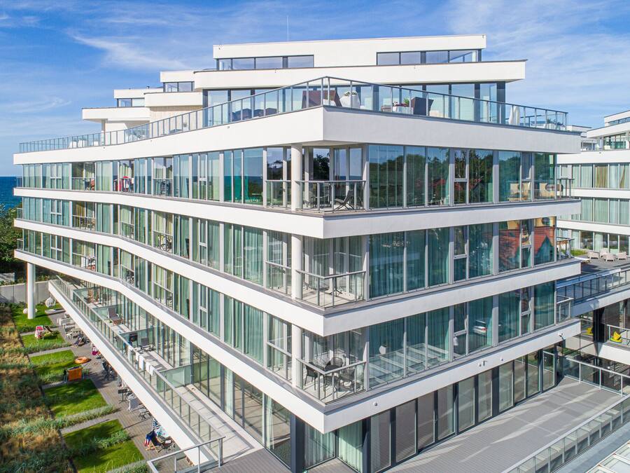 A modern multi-story building with large glass windows and balconies, located near a body of water.