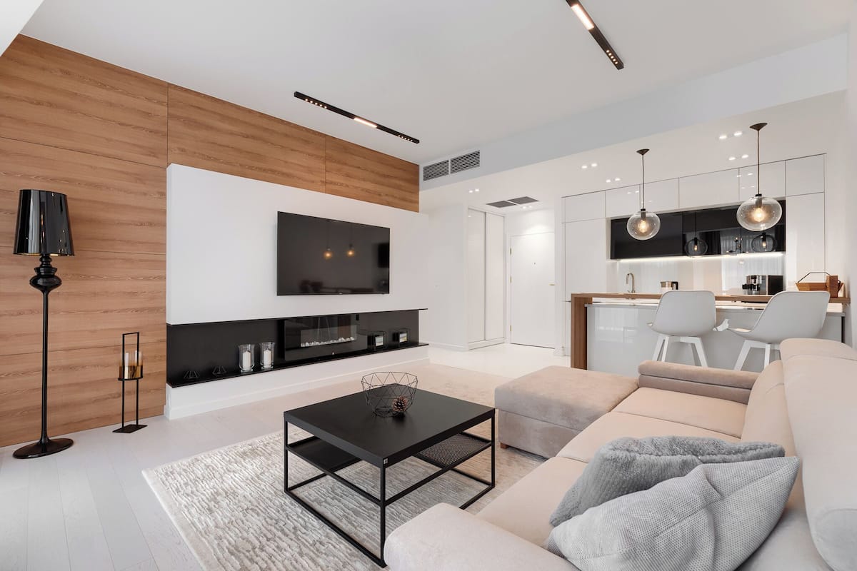 Ein modernes Wohnzimmer mit Flachbildfernseher, schwarzem Couchtisch, beiger Couch und einer Küchenzeile mit Barhocker.