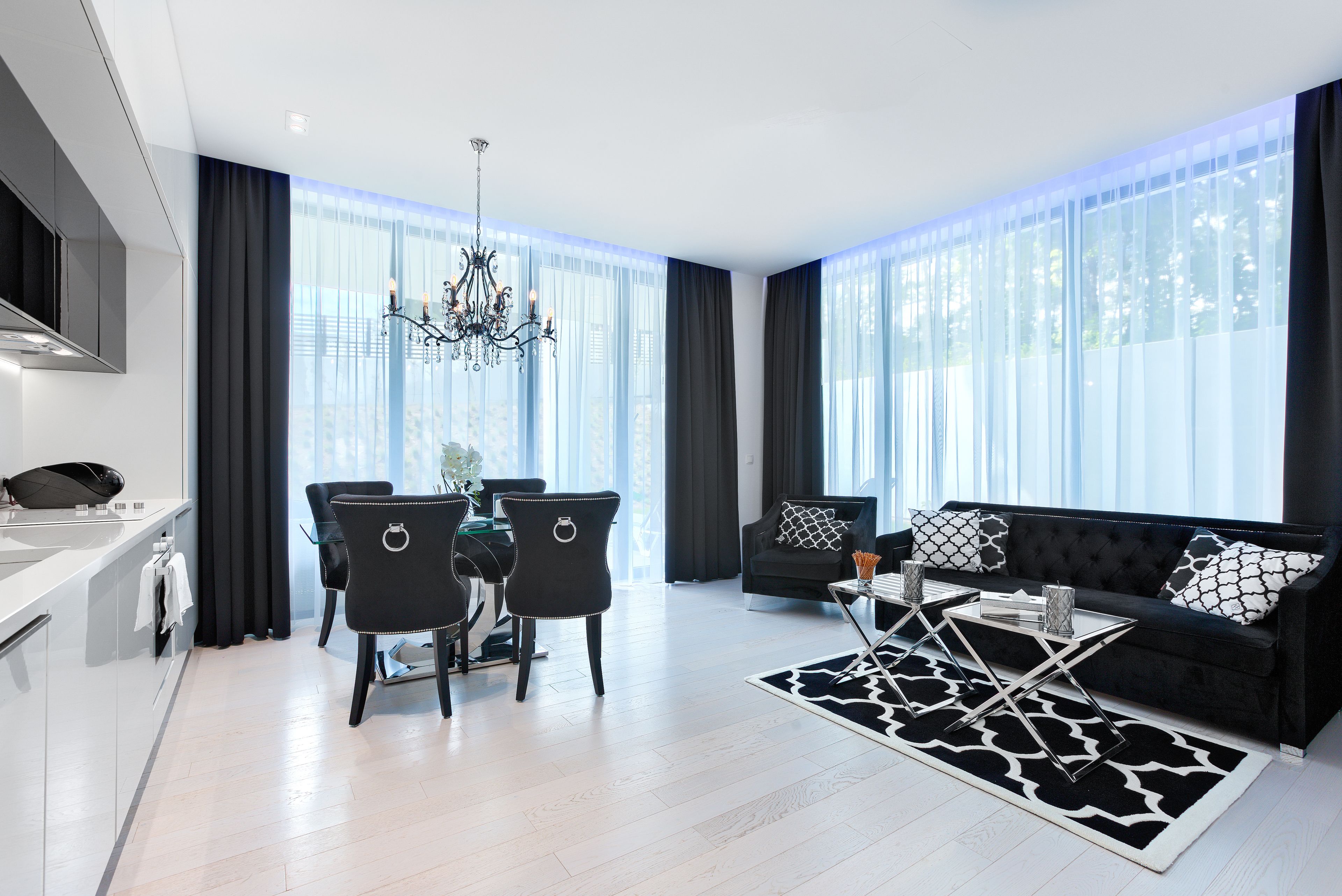 A modern living room with a black sofa, a dining table with chairs, and a chandelier.