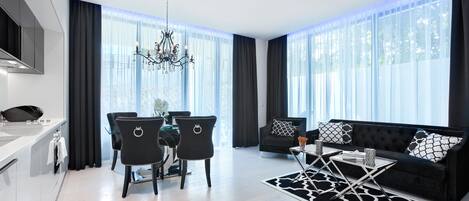 A modern living room with a black sofa, a dining table with chairs, and a chandelier.