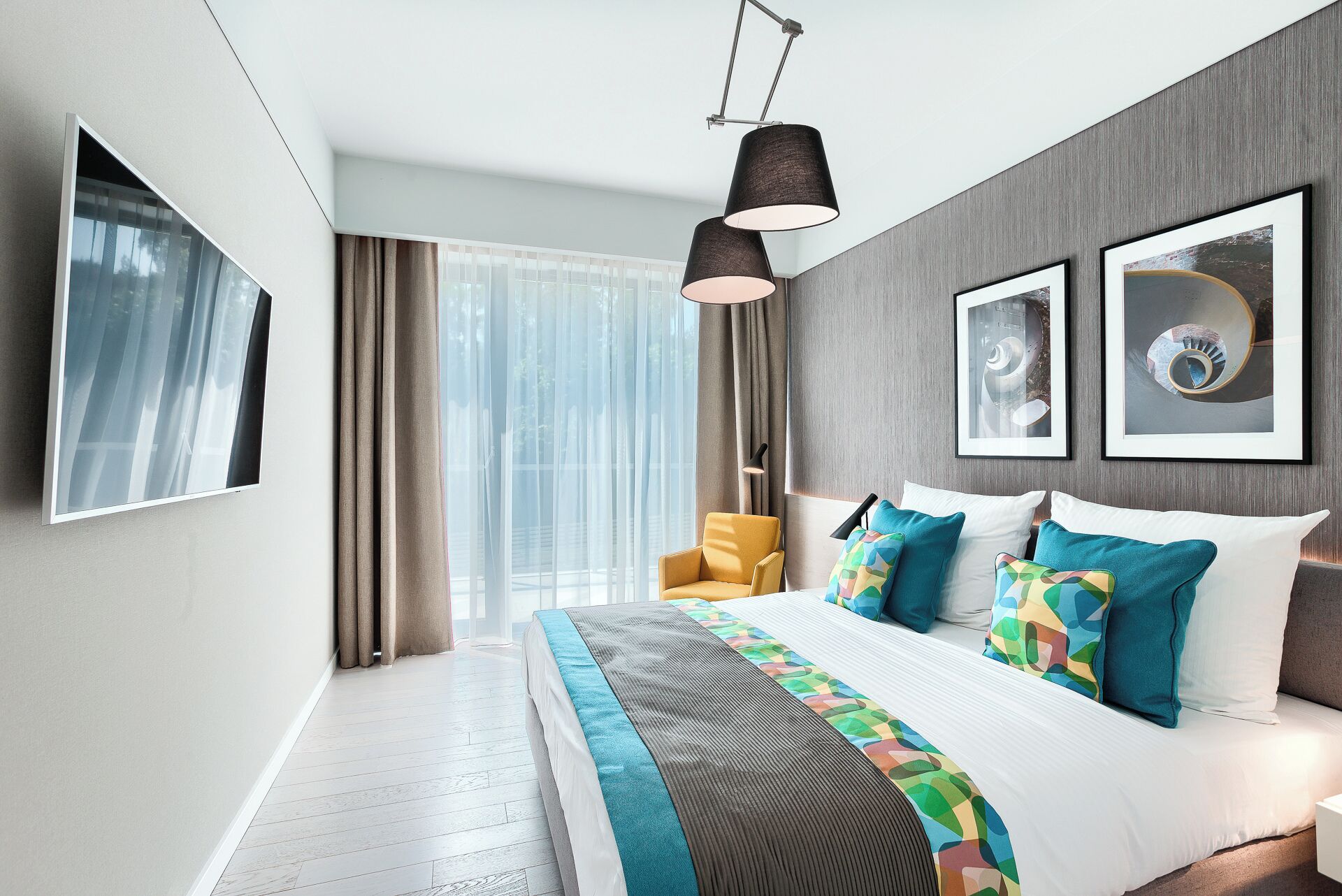 A modern hotel room with a large bed, a chair, a desk, and a view of the outdoors.