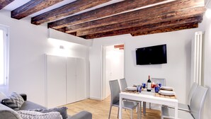 A modern living room with a wooden ceiling, a flat-screen TV, a dining table with chairs, and a sofa with cushions. - San Marco - Campo Manin by Wonderful Italy (Venice)