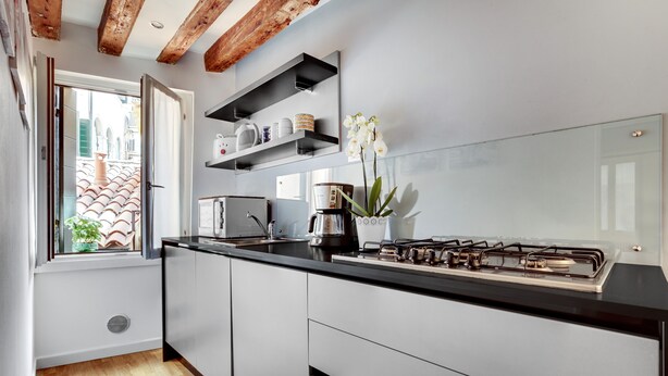 A modern kitchen with a gas stove, white cabinets, and a window with a view of a tiled roof. - San Marco - Campo Manin by Wonderful Italy (Venice)