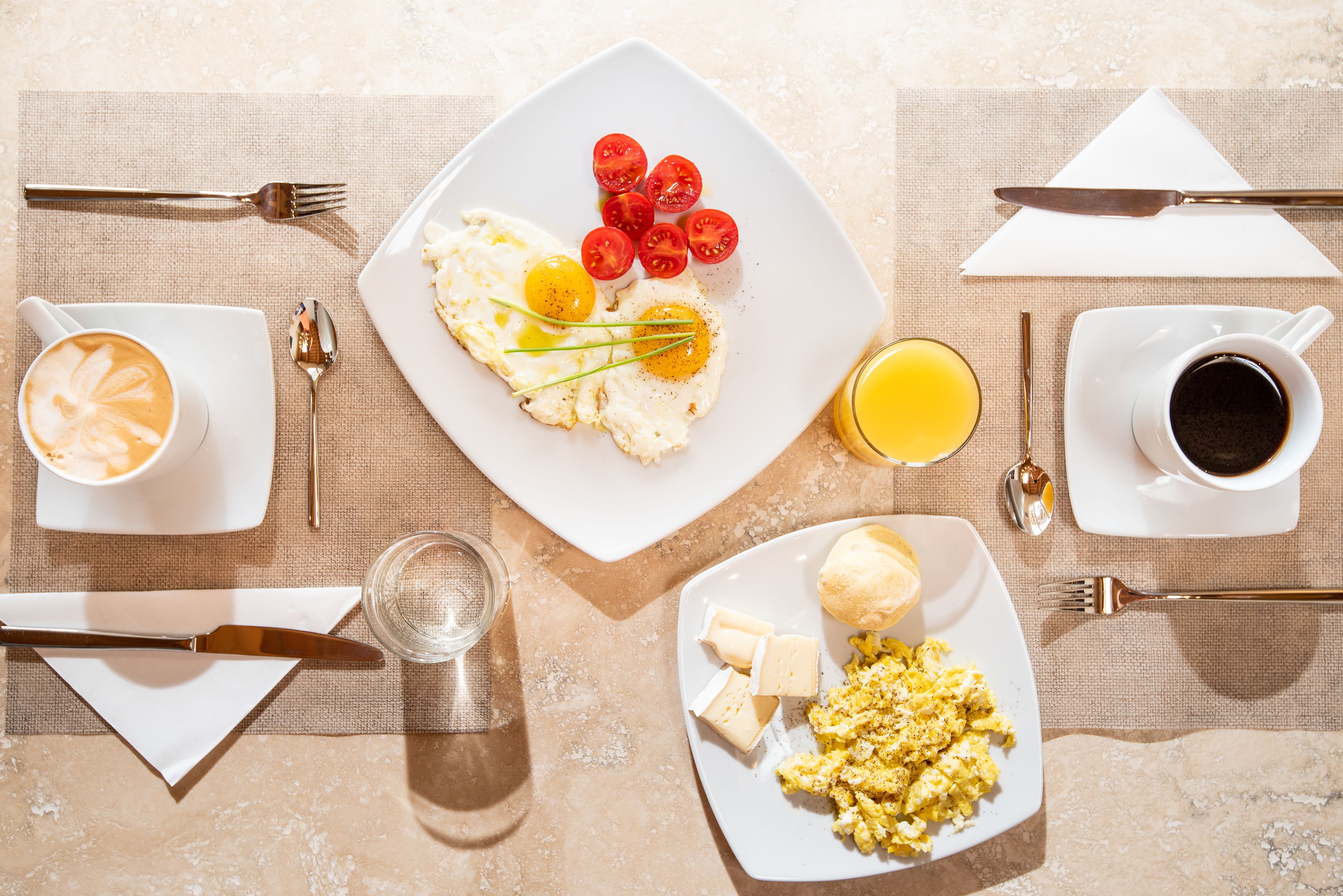 A breakfast setting with scrambled eggs, tomatoes, cheese, and coffee on a table.