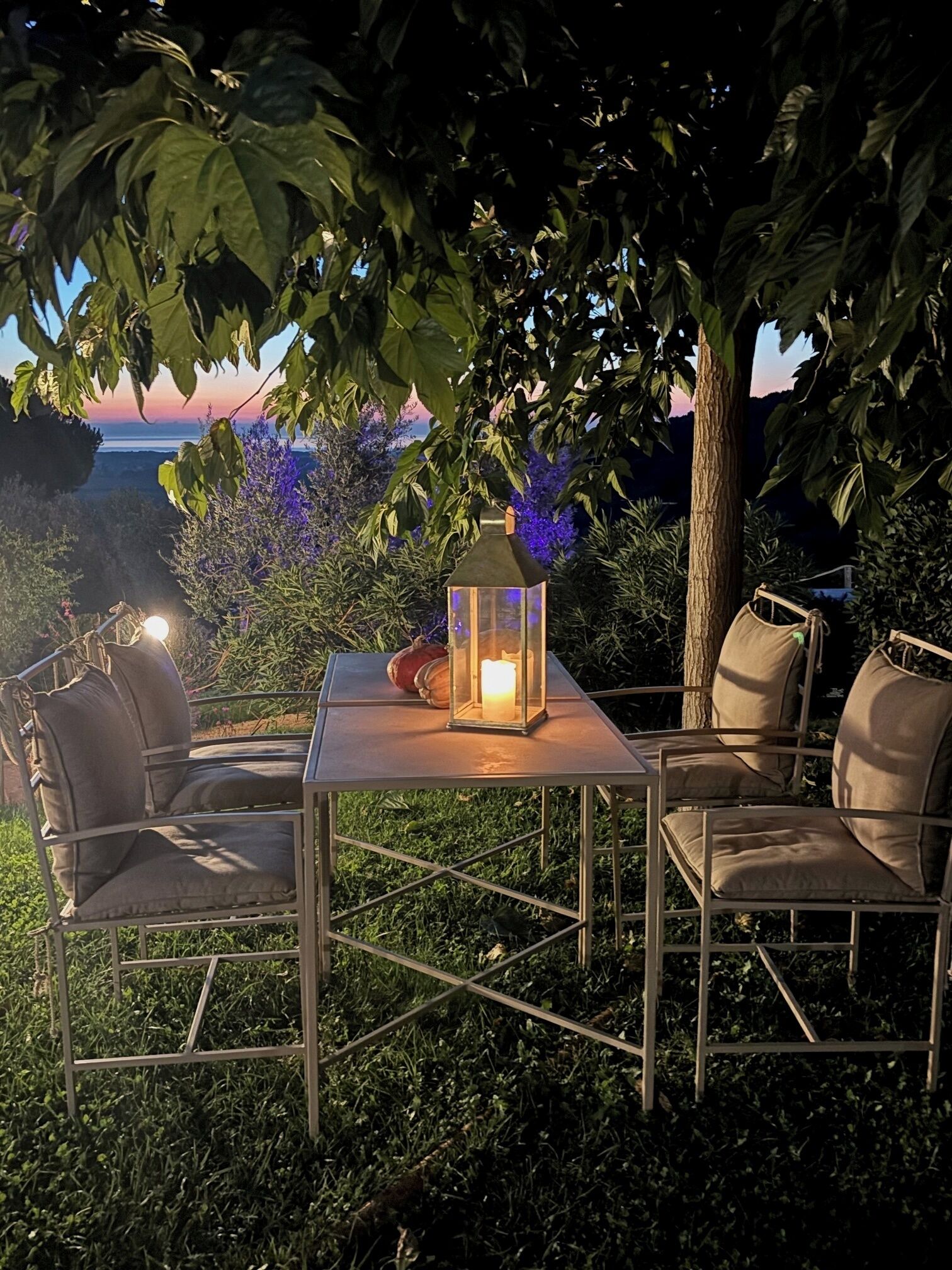 Un espacio al aire libre con mesa y sillas, un farol y vistas al atardecer.