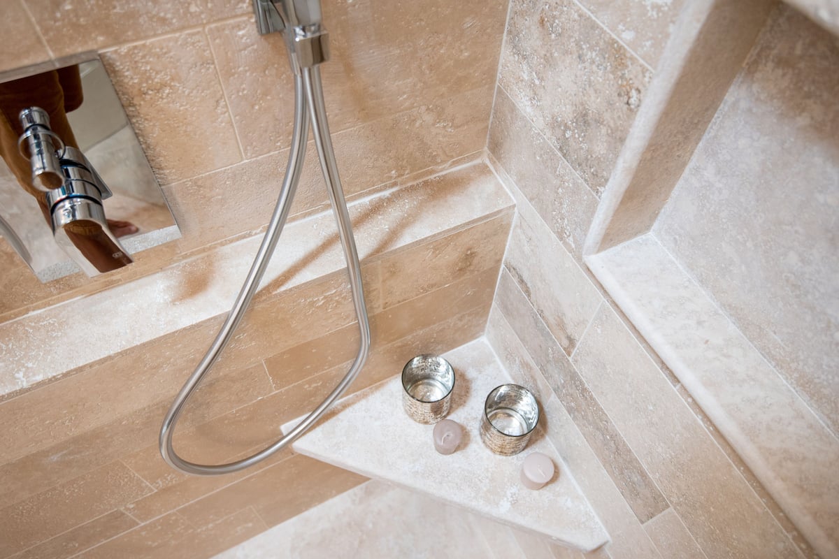 Un espace douche équipé d’un pommeau de douche à main et de deux récipients en verre vides placés sur une étagère.