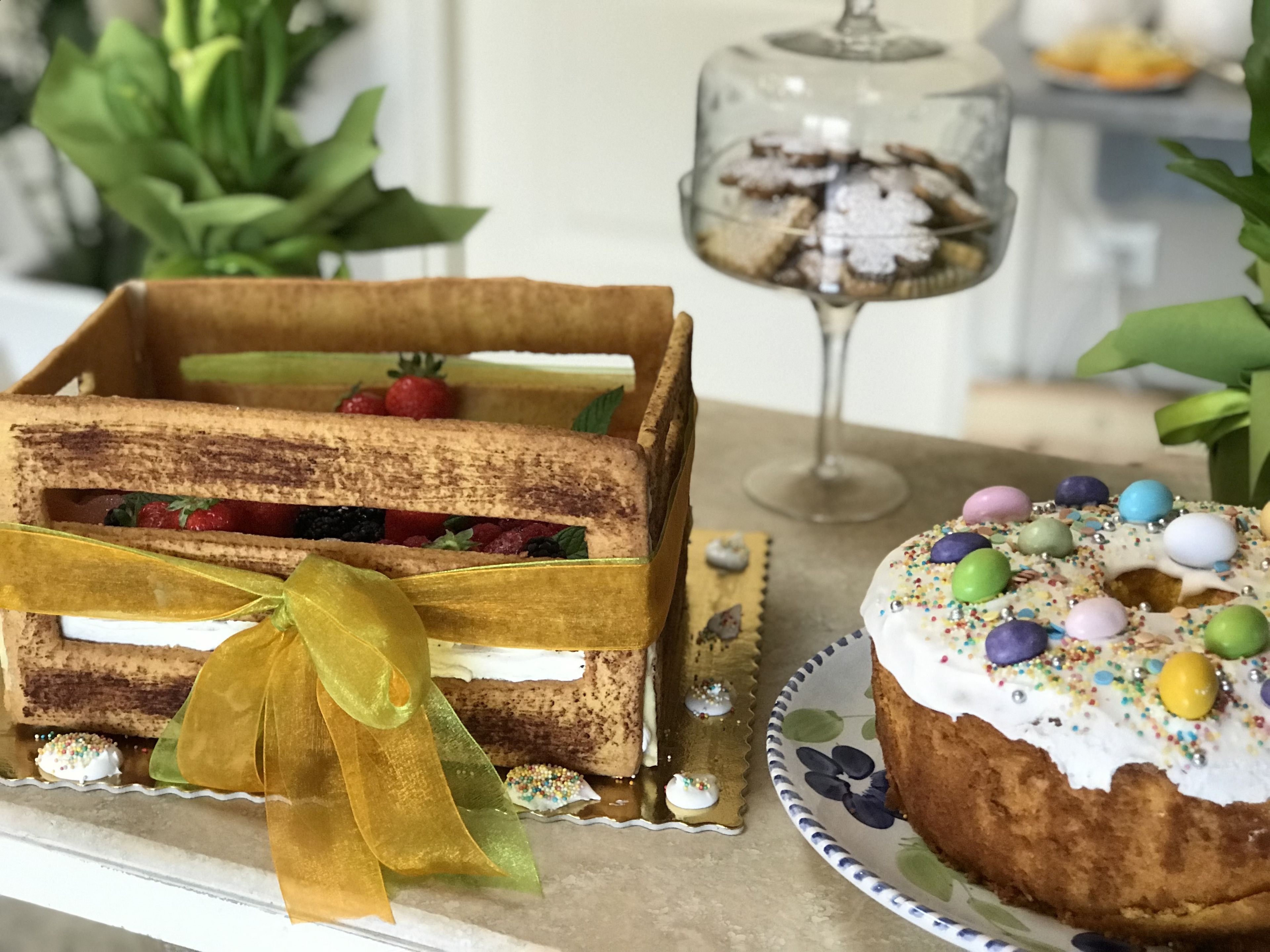 Una caja de madera con una cinta amarilla, llena de pasteles y un tarro de vidrio con más pasteles.