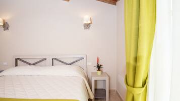Quarto com cama, duas arandelas, mesa de cabeceira com uma planta e cortina verde.