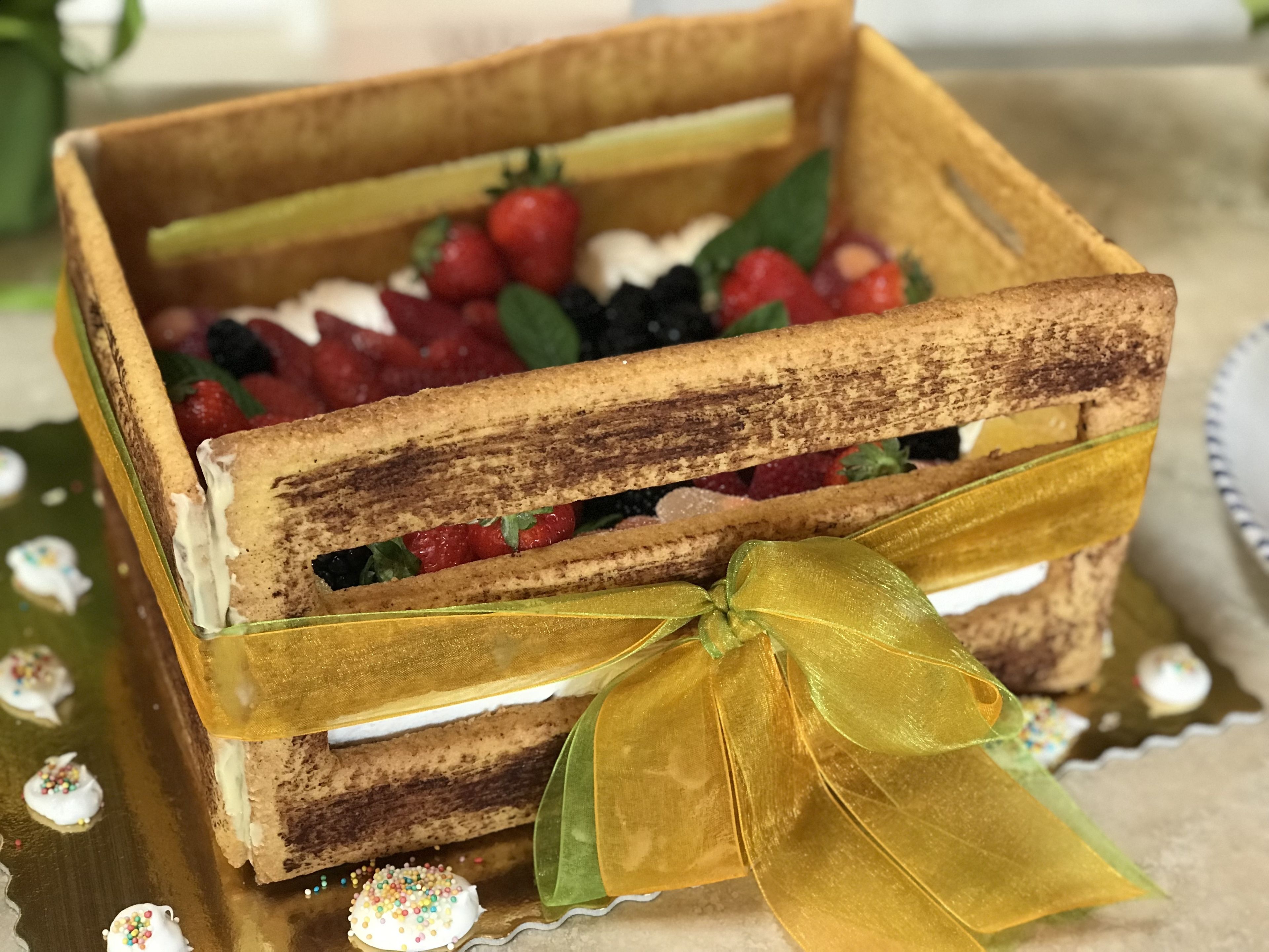 Una cassa di legno con un nastro dorato, che contiene dolci stratificati e frutti di bosco freschi.