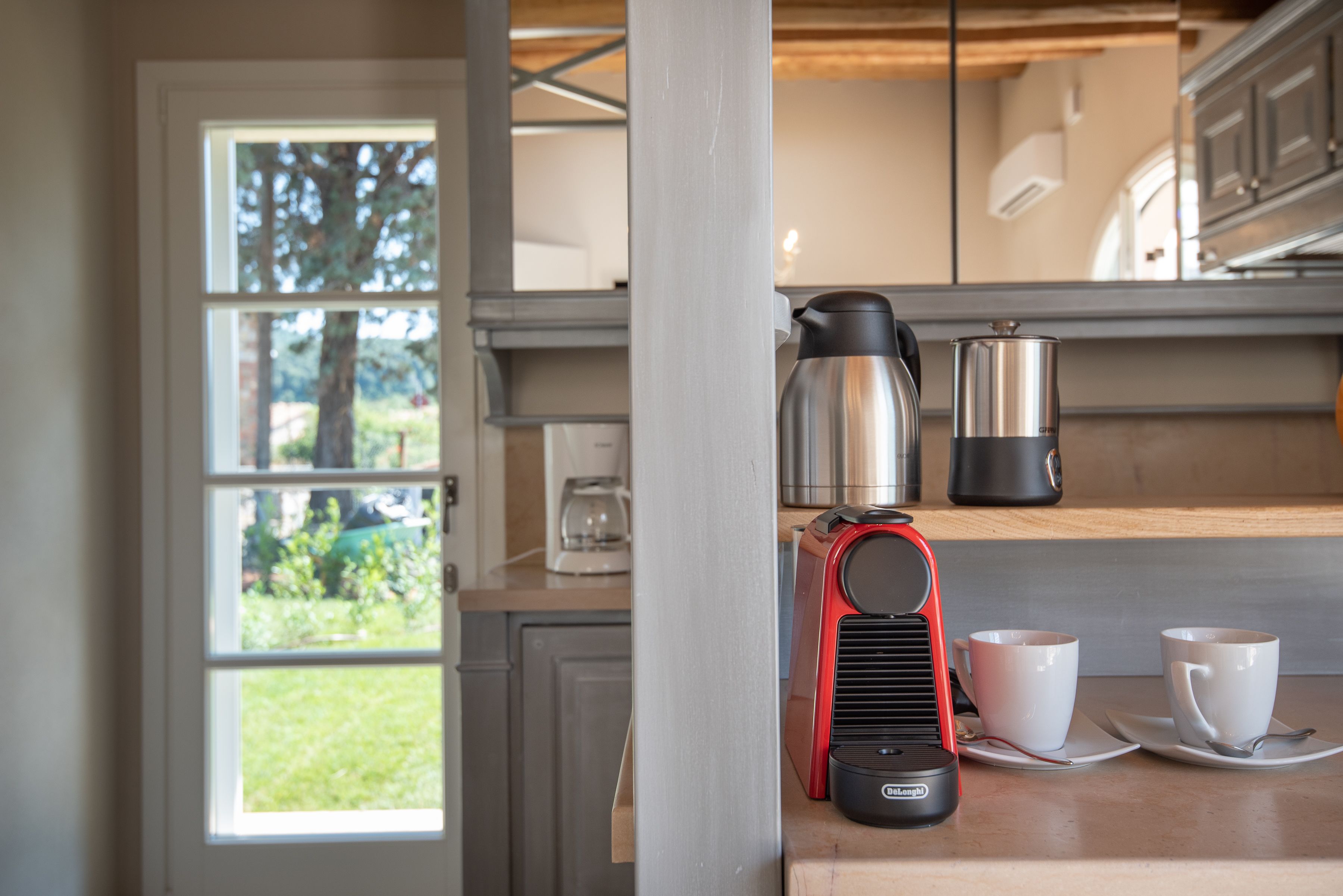A kitchen with a coffee maker, two cups, and a kettle on the counter.