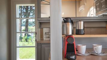 A kitchen with a coffee maker, two cups, and a kettle on the counter.
