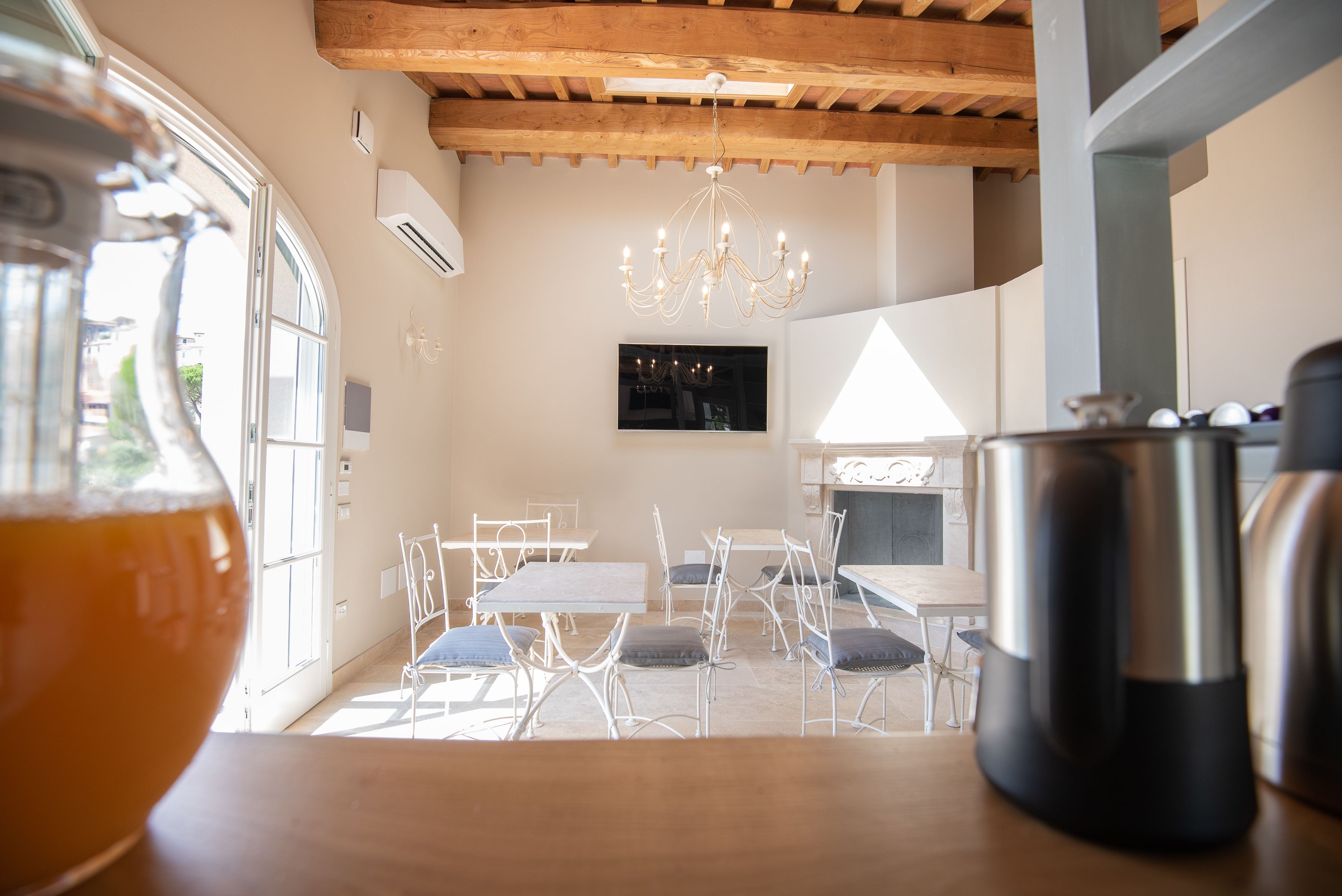 Un comedor con sillas y mesas de metal blanco, una araña y un ventanal grande.
