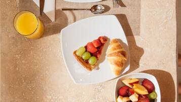 A breakfast setting with croissants, fruit, coffee, and juice on a table.