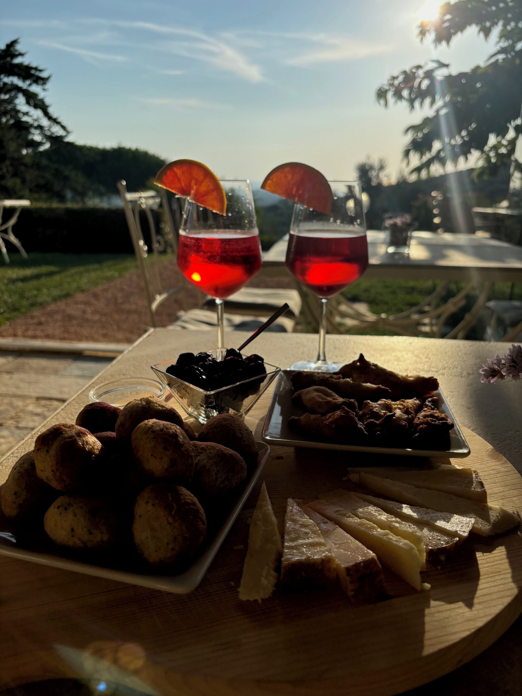 Un tavolo con due bicchieri di bevanda rossa, un piatto di biscotti e un vassoio di carne.
