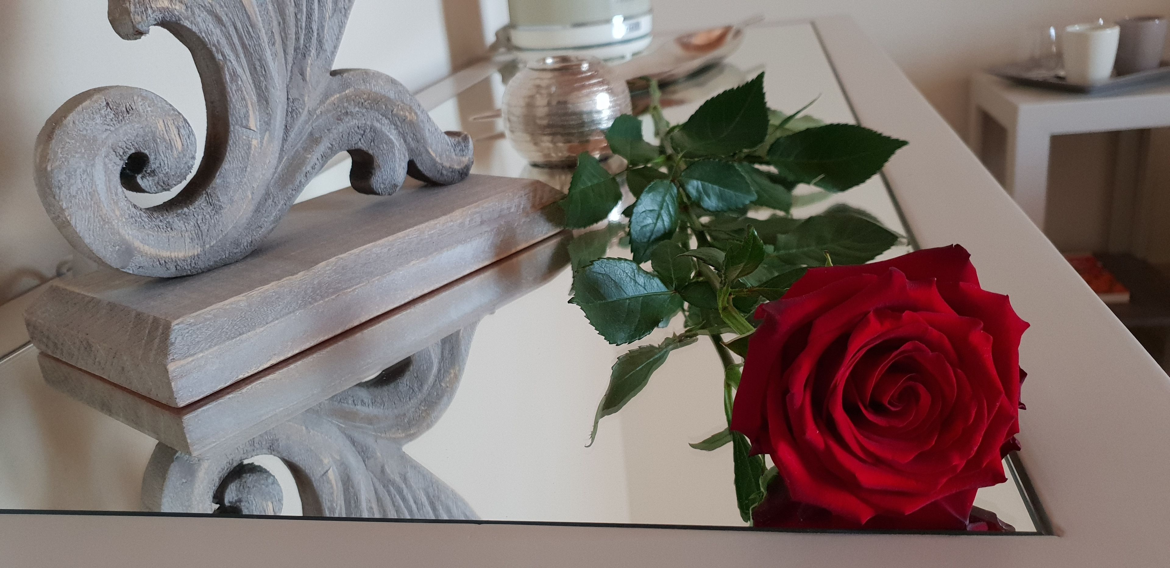 Una mesa con una escultura de metal decorativa, un florero de cristal con una rosa roja y un mantel blanco.