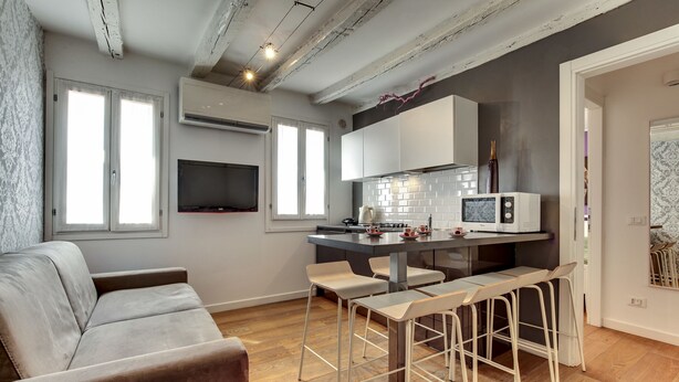 A modern kitchen with a dining area, featuring a sofa, bar stools, and a TV. - Ca' d'Oro Design by Wonderful Italy (Venice)
