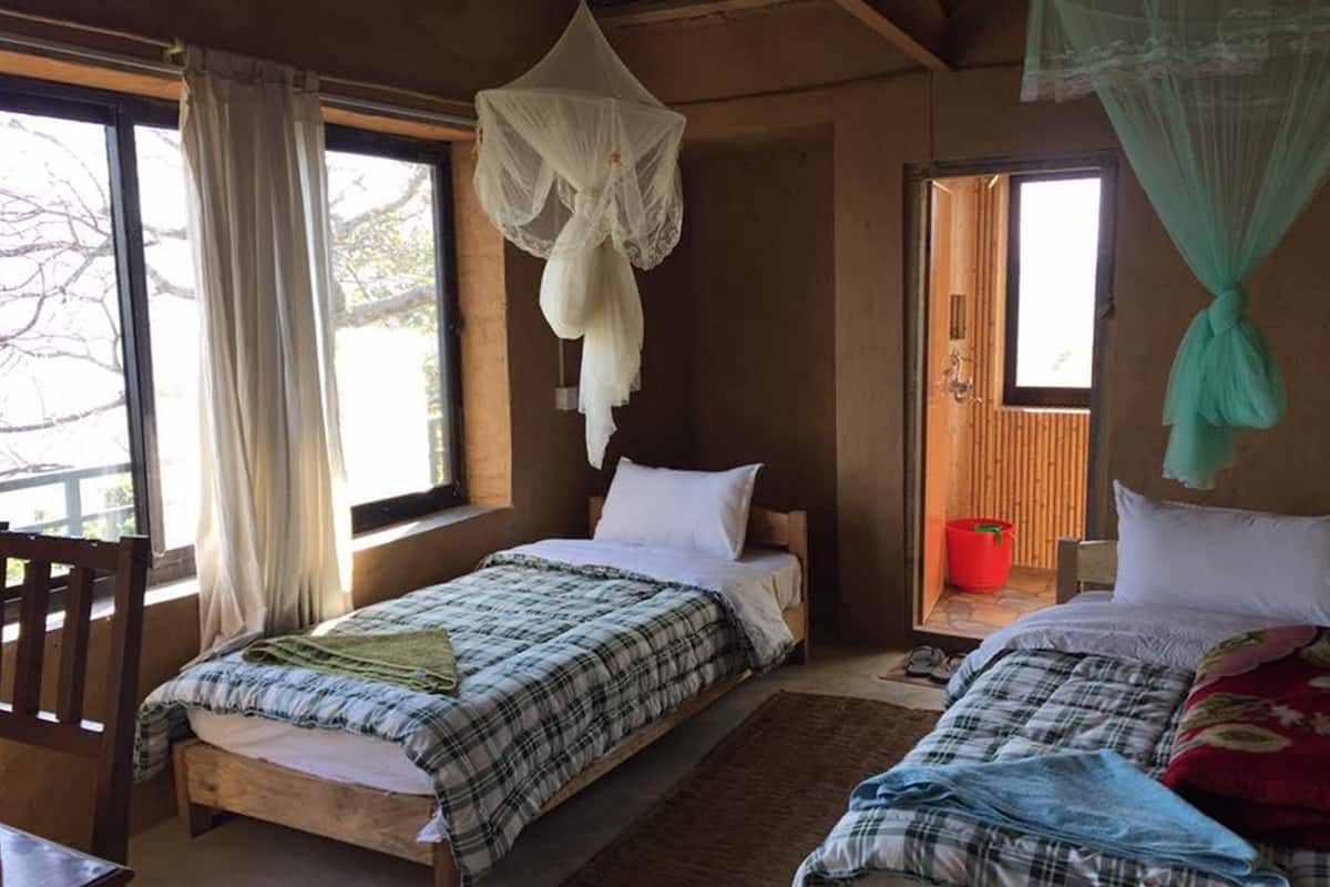 Une chambre avec deux lits, un plancher en bois, une fenêtre avec des rideaux et une moustiquaire.