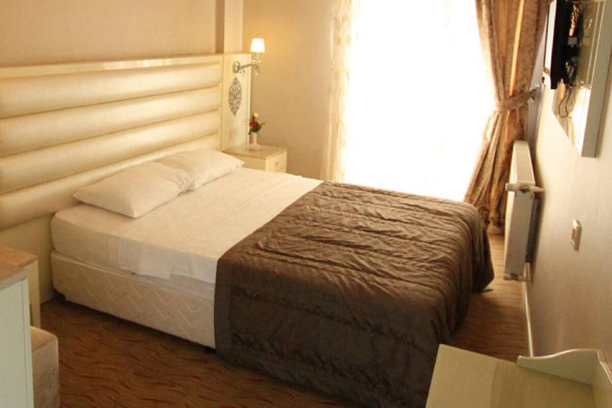 Une chambre d’hôtel avec un lit, des tables de chevet, une petite table, un vase avec des fleurs et une lampe.