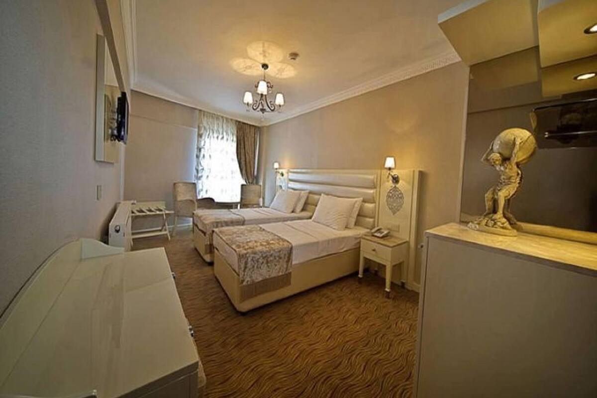 Une chambre d’hôtel comprenant un lit, deux tables de chevet, un bureau, une chaise, une armoire et un lustre.