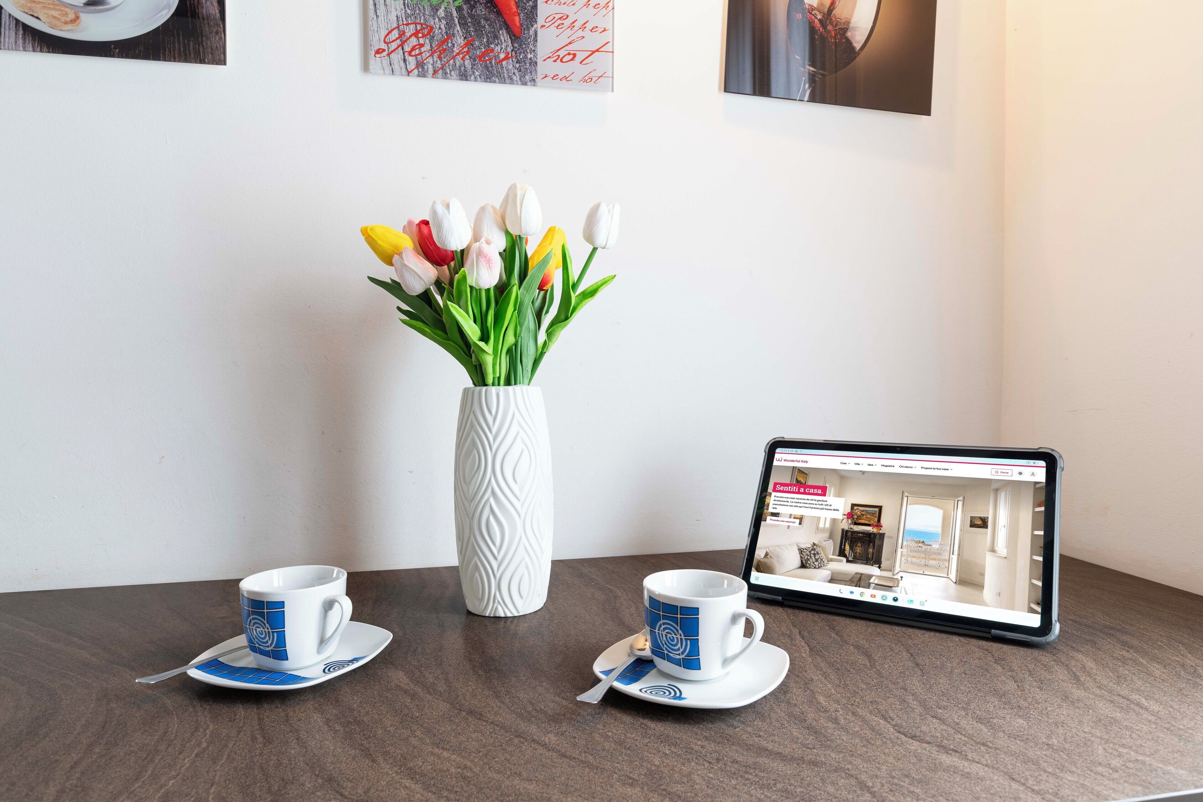 Een tablet toont een plattegrond, twee kopjes met schotels en een vaas met tulpen op een tafel.