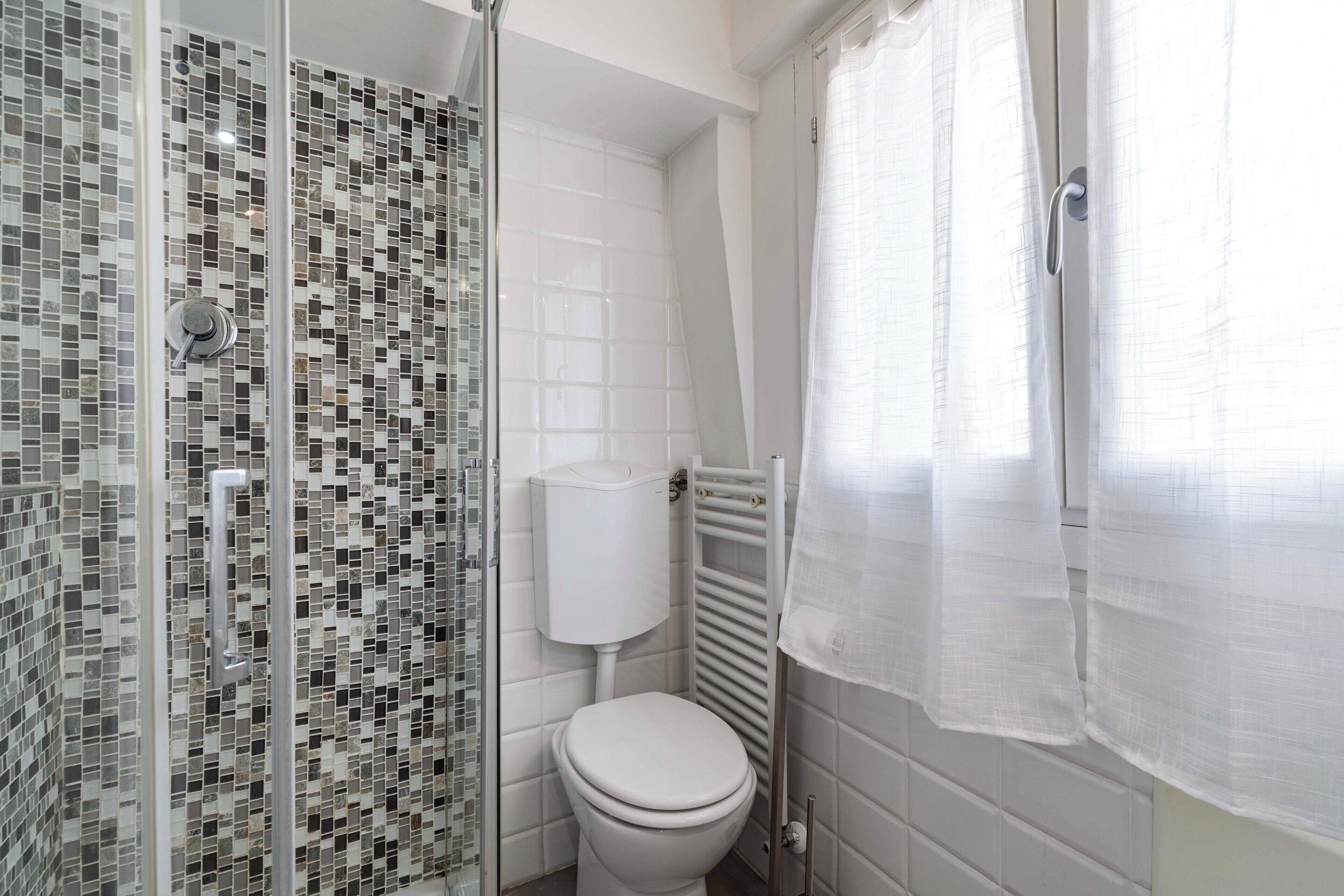 A bathroom with a shower, toilet, and a tiled wall.
