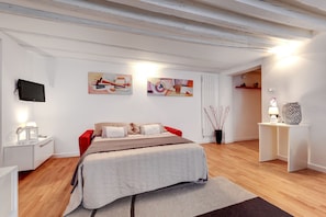 A modern bedroom with a bed, a TV, artwork, and a small table with a lamp.