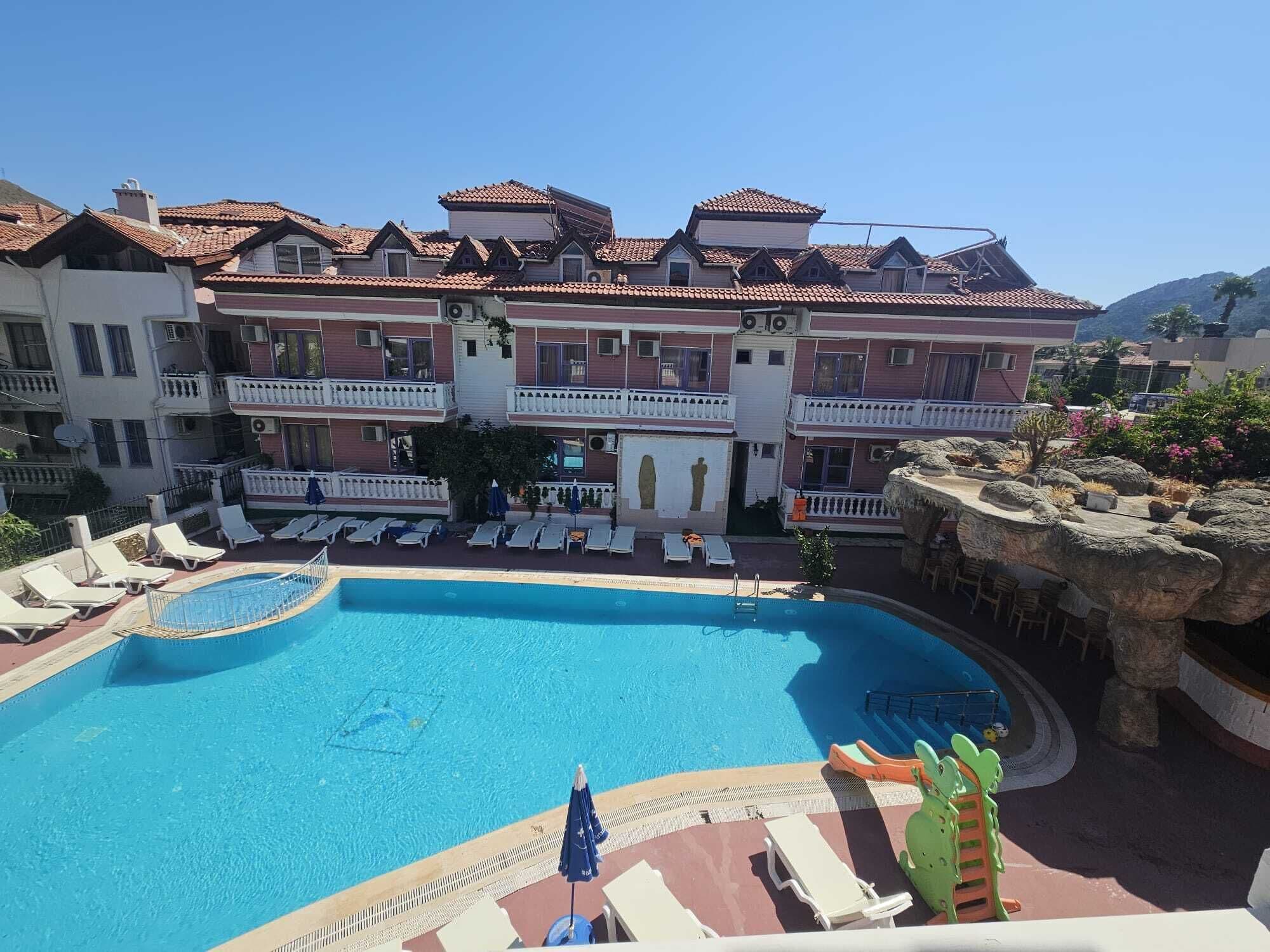 A hotel with a swimming pool, multiple balconies, and a view of the surrounding landscape.
