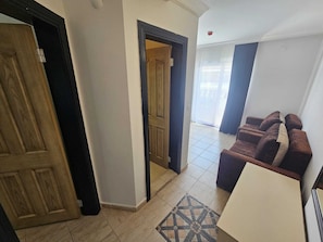 A hallway with a wooden door, a dark-framed door, and a tiled floor leading to a living area with a sofa and a patterned rug. - Bahar Apart (Marmaris)