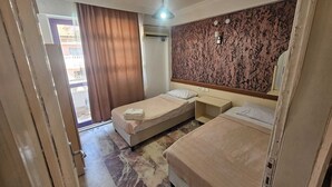 Habitación de hotel con dos camas, un espejo grande, ventilador de techo y vistas al exterior.