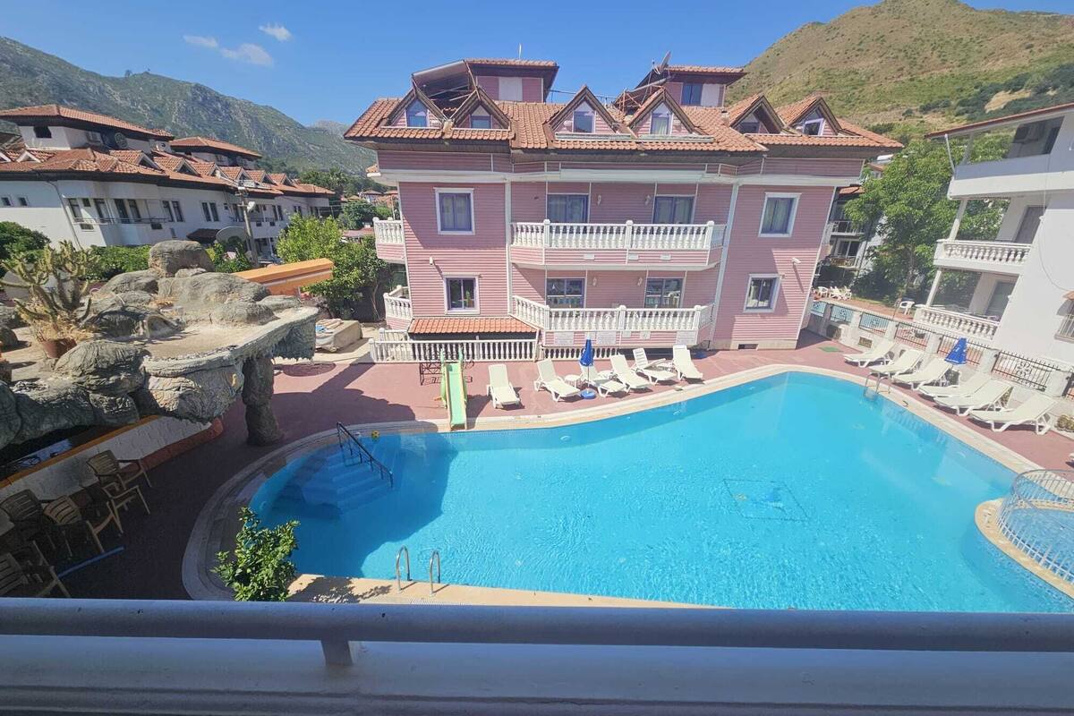 Un hôtel doté d’une piscine, d’un balcon avec des chaises longues et offrant une vue sur un paysage montagneux.